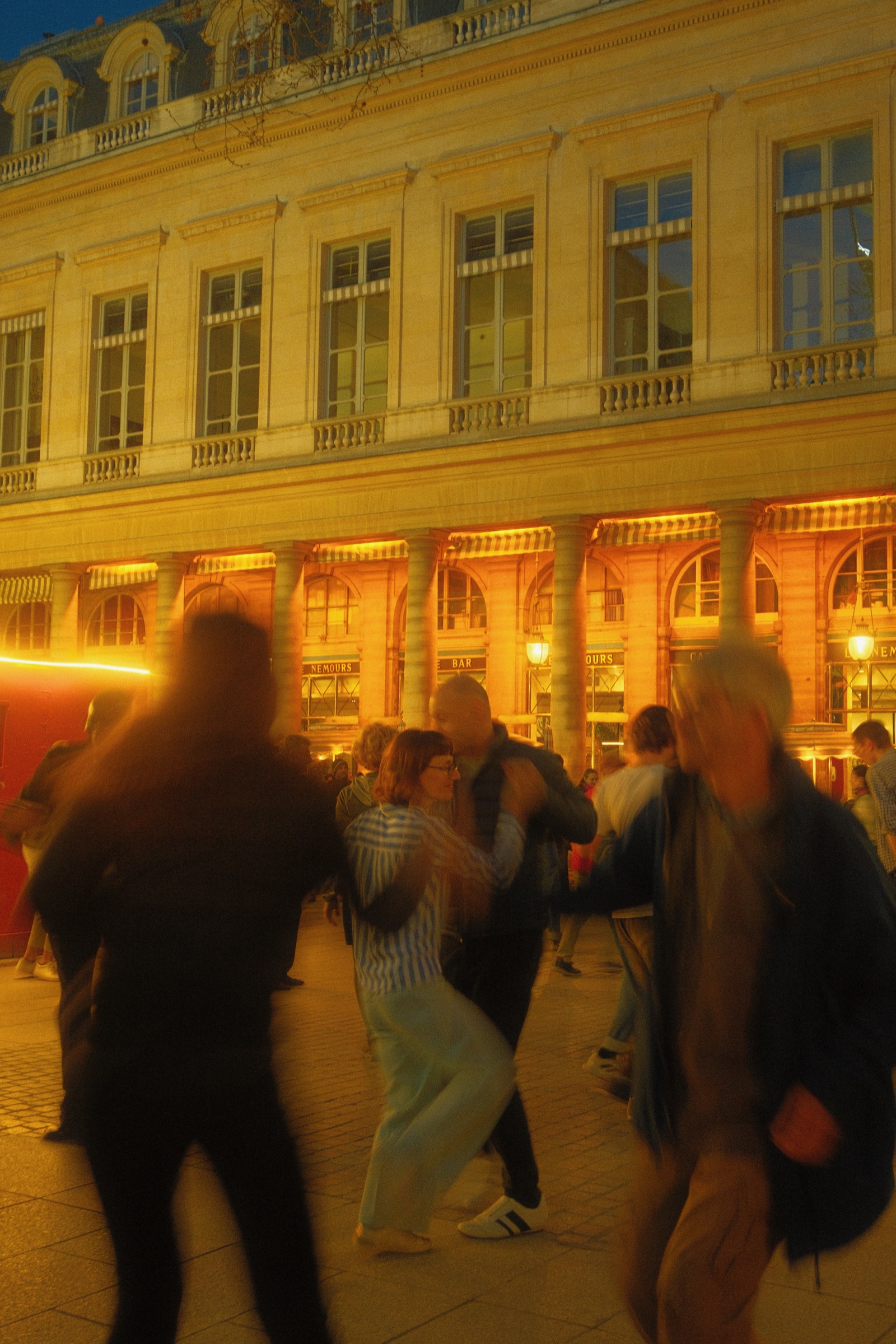Dancers at dusk in front of the lit colonnade of the Palais-Royal